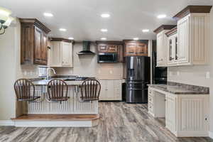 Kitchen featuring light wood finished floors, stainless steel appliances, a peninsula, wall chimney range hood, and stacked washer / dryer