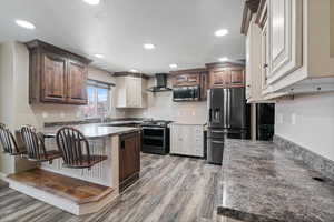 Kitchen with a peninsula, appliances with stainless steel finishes, a kitchen bar, light wood-type flooring, and wall chimney exhaust hood
