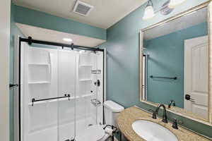 Bathroom with a textured ceiling, a shower stall, visible vents, toilet, and vanity