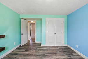 Unfurnished bedroom featuring a textured ceiling, baseboards, dark wood-style floors, and a closet