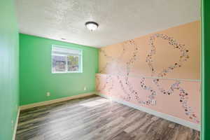 Empty room featuring a textured ceiling, visible vents, wood finished floors, and baseboards