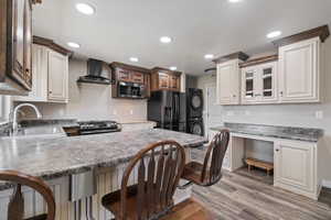 Kitchen with a sink, appliances with stainless steel finishes, stacked washer and clothes dryer, wall chimney exhaust hood, and a peninsula