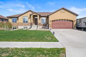 Ranch-style home with a garage, stucco siding, a front yard, and stone siding