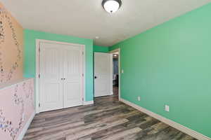 Unfurnished bedroom featuring a textured ceiling, wood finished floors, baseboards, and a closet