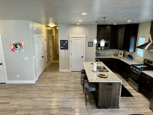 Kitchen featuring wall chimney exhaust hood, light wood-style flooring, a sink, appliances with stainless steel finishes, and a breakfast bar area