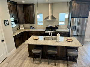 Kitchen featuring dark brown cabinets, wall chimney exhaust hood, baseboards, light wood-style flooring, and appliances with stainless steel finishes