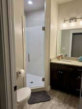 Bathroom with a shower stall, toilet, vanity, and wood finished floors