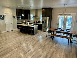 Kitchen with a breakfast bar, light wood-type flooring, wall chimney exhaust hood, and appliances with stainless steel finishes