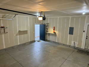 Garage featuring a garage door opener, electric panel, and baseboards