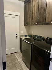 Clothes washing area with light wood finished floors, washer and clothes dryer, and cabinet space