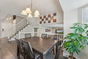 Dining space with a textured ceiling, vaulted ceiling, a notable chandelier, wood finished floors, and stairs