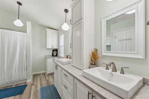Full bath featuring baseboards, wood finished floors, a sink, and double vanity