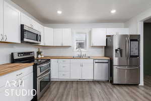 Kitchen with a sink, wood finished floors, wooden counters, stainless steel appliances, and white cabinets