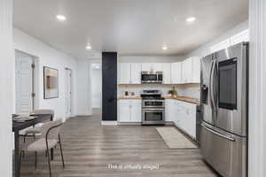 Kitchen featuring light wood finished floors, a sink, recessed lighting, custom butcher board counters, white cabinetry, and appliances with stainless steel finishes