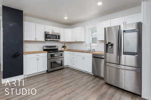 Kitchen with custom butcher block counters, light wood-type flooring, appliances with stainless steel finishes, and a sink and chalkboard wall.