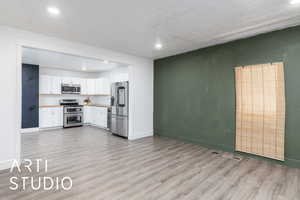 open concept living area with light wood-style flooring, light  custom, butcher board countertops, white cabinets, baseboards, and appliances with stainless steel finishes