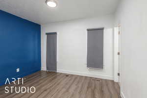 Empty room featuring wood finished floors, a textured ceiling, baseboards, and visible vents, cooling unit, closet and en suite bathroom