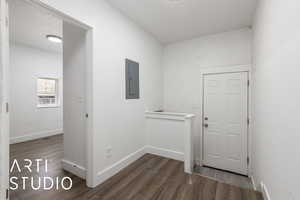 Corridor featuring wood  style finished floors, baseboards, and electric panel, and back door and stairs to basement