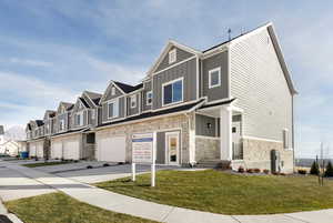 Townhome / multi-family property with board and batten siding, a residential view, stone siding, a front yard, and a garage