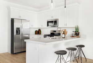 Kitchen featuring a breakfast bar, stainless steel appliances, white cabinets, light wood finished floors, and a peninsula