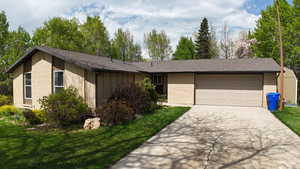 Ranch-style home featuring a front lawn, driveway, an attached garage, brick siding, and roof with shingles