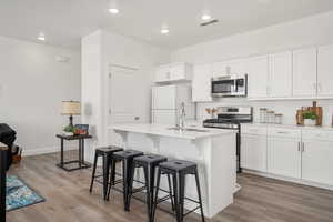 Kitchen with white cabinetry, a sink, appliances with stainless steel finishes, visible vents, and an island with sink