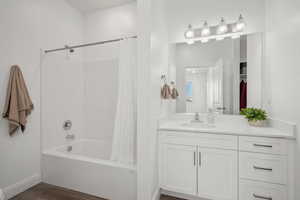 Bathroom featuring vanity, shower / bathtub combination with curtain, wood finished floors, and baseboards