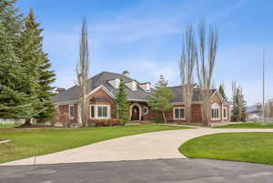 View of front of property with a chimney, a front yard, brick siding, and curved driveway