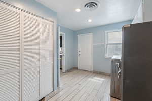 Kitchen with independent washer and dryer, freestanding refrigerator, white cabinets, baseboards, and visible vents