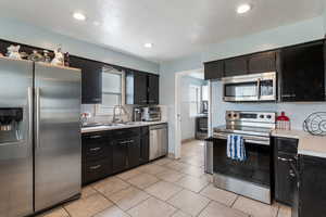 Kitchen featuring stainless steel appliances, dark cabinets, light countertops, and a sink