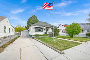 View of front of home with a front lawn, a garage, an outdoor structure, roof with shingles, and fence