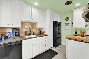 Kitchen with light wood-style flooring, white cabinets, black appliances, a sink, and baseboards