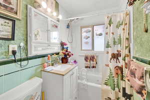 Bathroom featuring a wainscoted wall, wallpapered walls, shower / bath combo with shower curtain, toilet, and vanity