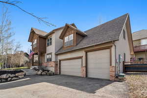 View of front of property featuring driveway, stone siding, roof with shingles, stucco siding, and fence
