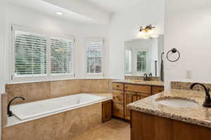 Bathroom featuring a bath, two vanities, a sink, and tile patterned floors