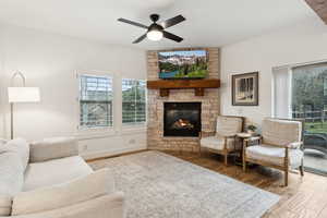 Living room featuring a stone fireplace, ceiling fan, wood finished floors, and visible vents