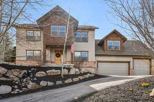 View of front of house featuring a shingled roof, stucco siding, driveway, and stone siding
