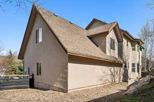 View of side of home with a shingled roof, stucco siding, and fence