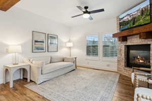 Living area with a ceiling fan, baseboards, wood finished floors, and a fireplace