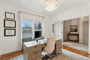 Office area with light wood-style floors, a notable chandelier, and baseboards
