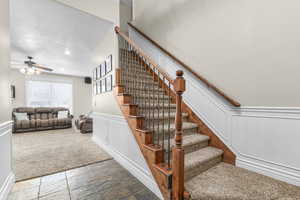Stairs featuring a decorative wall, wainscoting, stone tile flooring, a ceiling fan, and a textured ceiling