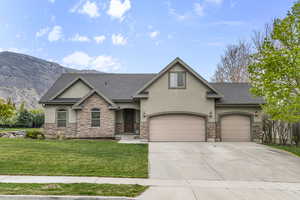 View of front of property with stucco siding, concrete driveway, a front yard, and stone siding