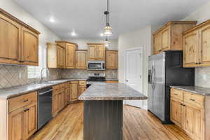 Kitchen featuring appliances with stainless steel finishes, light wood-style floors, a kitchen island, and a sink