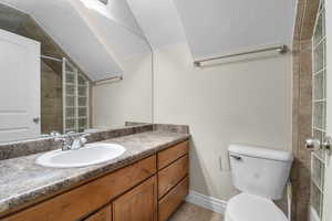 Bathroom featuring vanity, tile patterned floors, toilet, baseboards, and lofted ceiling