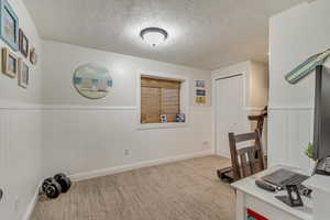 Carpeted office with a wainscoted wall, a textured ceiling, and baseboards