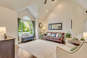 Living room featuring baseboards, high vaulted ceiling, wood finished floors, and ceiling fan