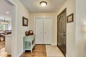 Foyer entrance with a textured ceiling, wood finished floors, a chandelier, and baseboards