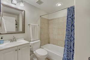 Bathroom featuring visible vents, toilet, shower / bath combination with curtain, and vanity