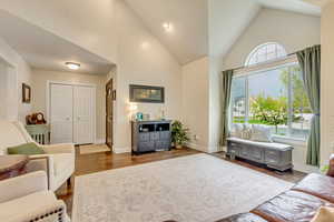 Living room featuring dark wood-style floors, high vaulted ceiling, and baseboards