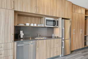 Kitchen with light brown cabinetry, stainless steel appliances, open shelves, and a sink